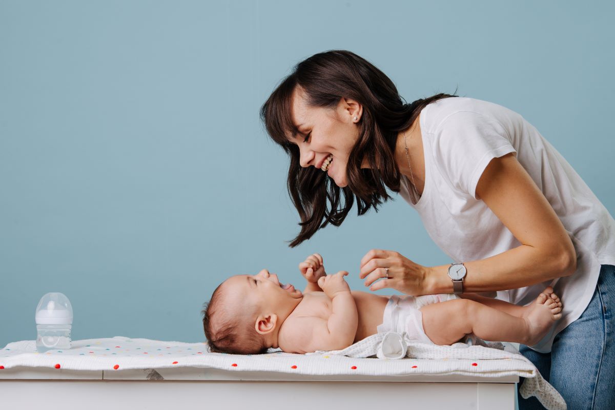Une mère sourit à son bébé qui fait ses dets allongé sur une table à langer.