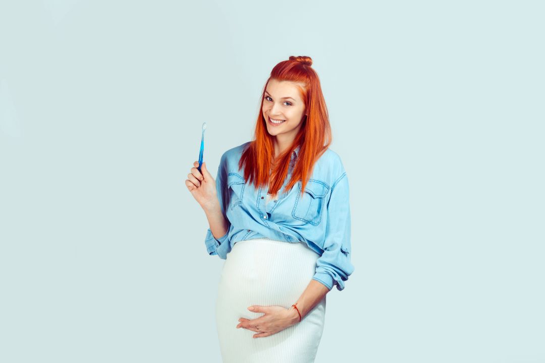 Une femme enceinte tient dans sa main une brosse à dents.